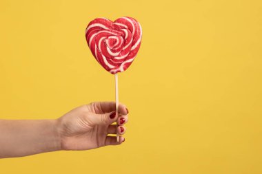 Kadının elinde iştah açıcı kalp şeklinde şekerler, kolunda büyük bir lolipop, şekerleme reklamları, şekerleme tatlısı yiyecekler. Sarı arka planda kapalı stüdyo çekimleri.