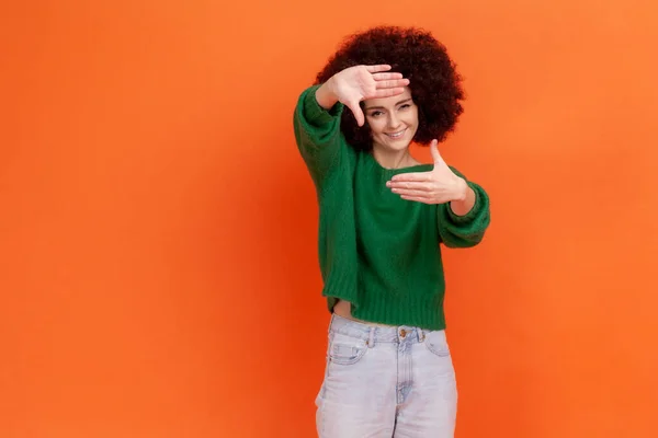 Smilende Kvinne Med Afrofrisyre Iført Grønn Avslappet Genser Gjennom Fingerrammen – stockfoto