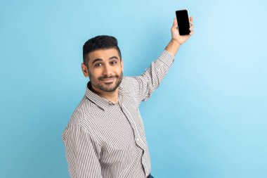 İş adamının görüntülü konuşma portresi, cep telefonuyla selfie çekmek, akıllı telefonu boş bir ekranla tutmak, çizgili gömlek giymek. Mavi arka planda kapalı stüdyo çekimi.