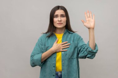 Ciddi vatansever bir kadın, el ele tutuşuyor, jüri üyesi mahkemede doğruyu söyleyeceğine yemin ediyor, onur ve vicdan sahibi, sıradan bir ceket giyiyor. Gri arka planda izole edilmiş kapalı stüdyo görüntüleri.