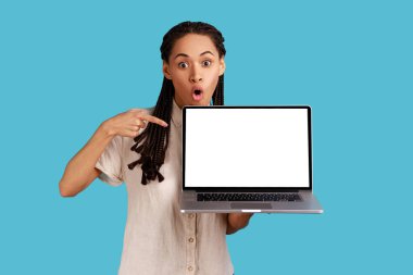 Rasta saçlı, etkilenmiş, korkmuş bir kadın ilgi ve heyecandan ağzı açar, dizüstü bilgisayarını boş ekranla gösterir, beyaz gömlek giyerek büyülendiğini hisseder. Mavi arka planda kapalı stüdyo çekimi.