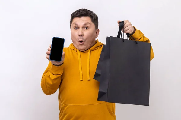 Zdumiewający Człowiek Trzymający Telefon Komórkowy Torby Zakupy Reklamujący Sklep Internetowy — Zdjęcie stockowe