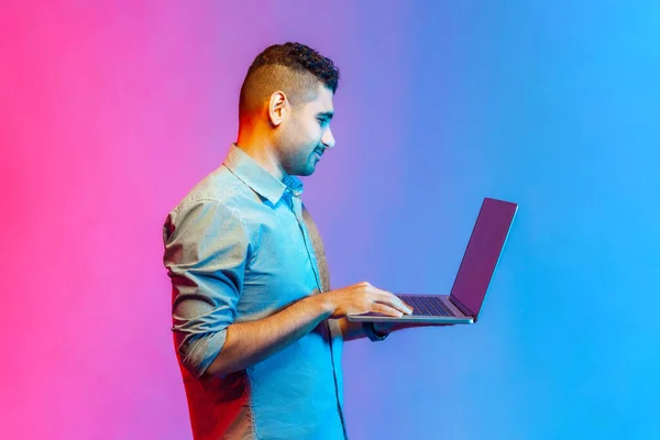 Tişörtlü Bir Adamın Elinde Dizüstü Bilgisayar Tutarken Yazarken Sosyal Ağlarda — Stok fotoğraf