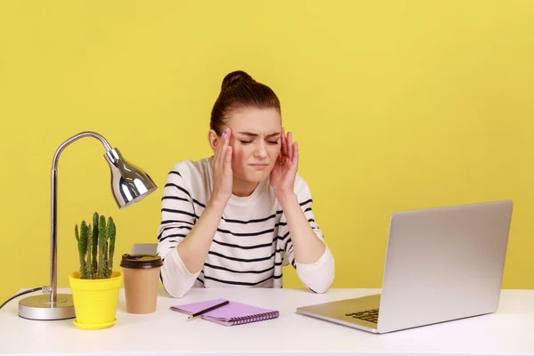 疲惫的年轻女性办公室经理带着笔记本电脑坐在工作场所 头痛医头 患有严重偏头痛 很沮丧 在黄色背景下隔离的室内工作室拍摄 — 图库照片