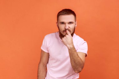 Yalancısın. Sakallı adamın burnu işaret eden portresi, yalan jestler gösteren, seni suçlayan ve kuşkulanan, pembe tişört giyen vücut dili. Turuncu arka planda kapalı stüdyo çekimleri.