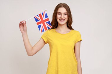 Sarı tişörtlü genç kızın portresi Birleşik Krallık 'ın seçmen birliğinin bayrağını taşıyor. 4 Haziran: İngiliz Bağımsızlık Günü. Gri arka planda izole edilmiş kapalı stüdyo görüntüleri.