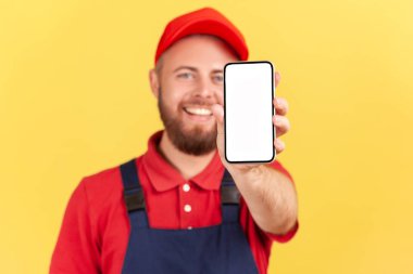 Memnuniyetle çalışan bir işçi ya da üniformalı bir tamirci cep telefonunu fotokopi alanının boş olduğu bir ekranda gösterip servisini tanıtıyor. Sarı arka planda kapalı stüdyo çekimleri.