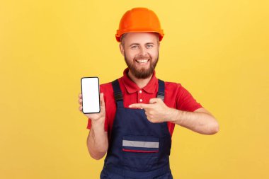 Tatmin olmuş müteahhit ya da üniformalı bir tamirci ve koruyucu kasklı cep telefonunda fotokopi alanı olan boş bir ekran gösteren, servisinin reklamını yapan. Sarı arka planda kapalı stüdyo çekimleri.