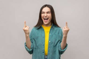 Angry excited woman standing with middle finger fuck sign and looking at camera with dissatisfied face, screaming, wearing casual style jacket. Indoor studio shot isolated on gray background.