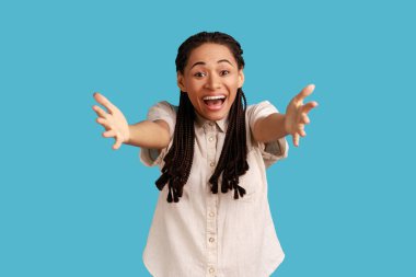 Rasta bukleli sevimli kadın ellerini uzatıyor ve doğrudan kameraya bakıyor, sana sarılıyor, en iyi arkadaşımı kucaklamak istiyorum, beyaz gömlek giyiyor. Mavi arka planda kapalı stüdyo çekimi.