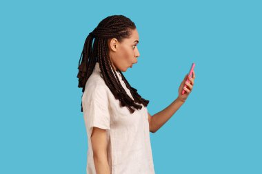 Siyah saçlı, şaşırmış bir kadın akıllı telefon ekranına bakıyor. Şaşırmış bir yüzle inanılmaz haberler okuyor. Bir şey karşısında afallıyor. Mavi arka planda kapalı stüdyo çekimi.