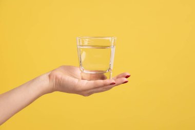 Avucunun içinde su olan el bardağını kapatan kadın. Temiz içecek reklamı. Su dengesini sağlamanın en iyi yolu. Sarı arka planda kapalı stüdyo çekimleri.