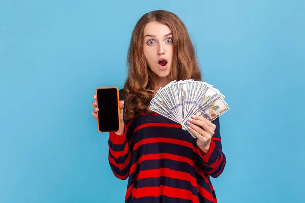 Zaszokowana Kobieta Nosząca Sweter Paski Pokazujący Dolary Smartfon Pustym Ekranem — Zdjęcie stockowe