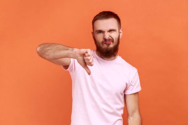 Kötü kaliteyi eleştirenin portresi, hoşnutsuz davranışlar gösteren, onaylamadığını belirten, pembe tişört giyen. Turuncu arka planda kapalı stüdyo çekimleri.