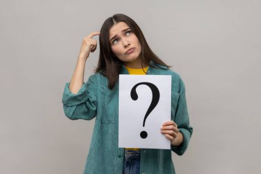 Düşünceli, düşünceli bir kadının portresi. Elinde soru işareti olan bir kağıt tutuyor. Sorunu çözmeyi düşünüyor. Gri arka planda izole edilmiş kapalı stüdyo görüntüleri.