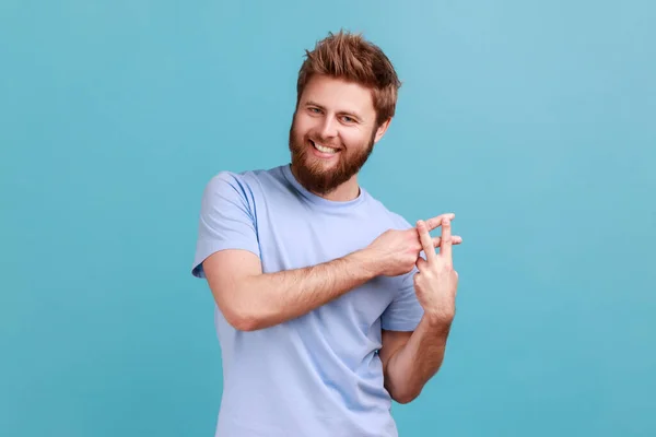 Internet trends. Portrait of satisfied smiling bearded man crossing fingers to make hashtag sign and looking at camera with toothy smile. Indoor studio shot isolated on blue background.