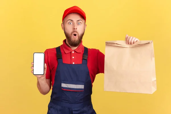 Otroligt Överraskad Leverans Man Håller Papper Paket Och Visar Mobiltelefon — Stockfoto