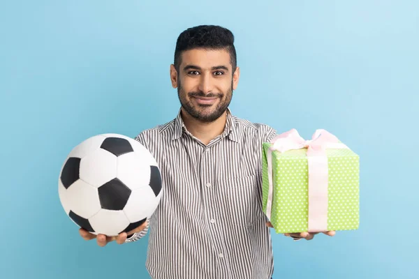 満足した幸せなビジネスマンの肖像画カメラを見て笑みを浮かべて立って サッカーボールと現在のボックスを保持し 縞模様のシャツを着ている 青い背景に隔離された屋内スタジオショット — ストック写真