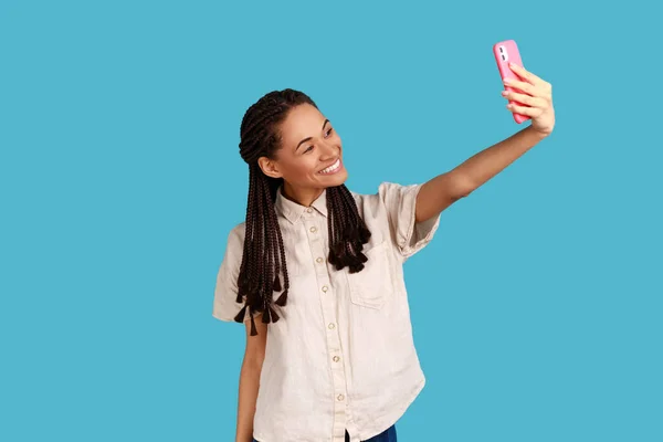 年轻可爱的女人带着黑发 看着智能手机的摄像头 自拍肖像 直播直播 穿着白衬衫 室内拍摄被蓝色背景隔离 — 图库照片