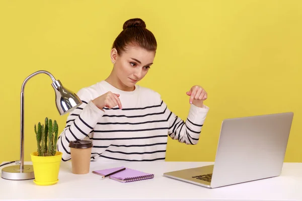 严肃的女人坐在工作场所 看着笔记本电脑的显示屏 指指点点 控制和要求在截止日期前完成工作 在黄色背景下隔离的室内工作室拍摄 — 图库照片
