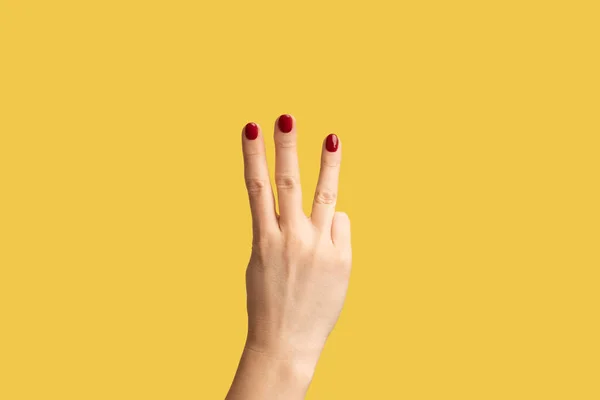 Profile side view closeup of woman hand with red manicure showing number 3 three with hands. Indoor studio shot isolated on yellow background.