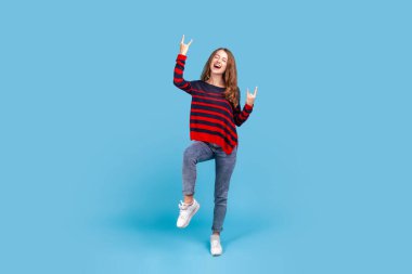 Evet, bu delilik! Heyecanlı bir kadın rock 'n roll el hareketi, punk işareti, kükreyen ve çığlıklar atan agresif müzikten zevk alan. Mavi arka planda kapalı stüdyo çekimi.