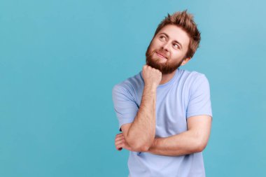 Gülümseyen mutlu sakallı bir adamın portresi. Dalgın bir ifadeyle başka tarafa bakıyor. Hoş düşünceler kuruyor, hayal kuruyor ve dilek tutuyor. Mavi arka planda kapalı stüdyo çekimi.