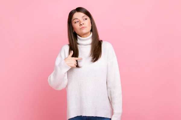 Portrait of confident female pointing at herself, feeling proud and self-important, having big ego, wearing white casual style sweater. Indoor studio shot isolated on pink background.