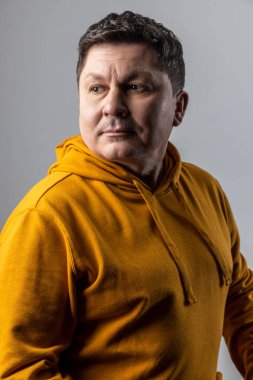 Yakışıklı, düşünceli orta yaşlı bir adamın portresi düşünceli görünüyor, başka tarafa bakıyor, derin düşünceler içinde, şehir tarzı kapüşonlu bir şey giyiyor. Gri arka planda izole edilmiş kapalı stüdyo görüntüleri.