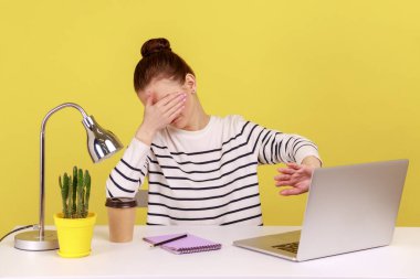 Buna daha fazla bakmak istemiyorum. Kafası karışmış bir kadın elleriyle gözlerini kapatıyor, dizüstü bilgisayardan utanç verici içerikleri izlemekten kaçınıyor, merkez ofisten çalışıyor. Sarı arka planda kapalı stüdyo çekimleri.