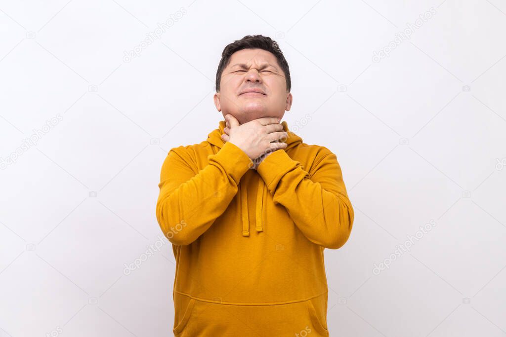 Portrait of flu-sick man clasping neck feeling unwell, suffering sore throat and inflamed tonsils, unbearable pain, wearing urban style hoodie. Indoor studio shot isolated on white background.