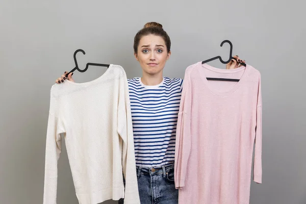 Portrait Confused Puzzled Woman Wearing Striped Shirt Holding Two Shirts — стоковое фото