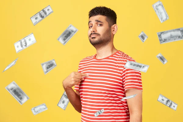 This is rich man. Portrait of arrogant self-confident man pointing at chest, looking proud and egoistic. money falling and he is rich. indoor studio shot isolated on yellow background
