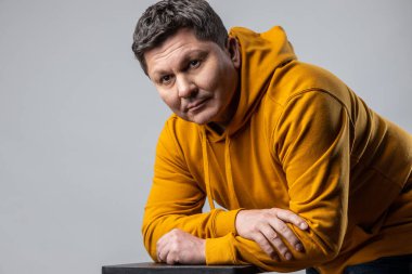 Sakin, orta yaşlı, düşünceli bakışları, güzelliği, moda portresi olan, kentsel kapüşonlu giyinmiş, kameraya bakan çekici bir adam. Gri arka planda izole edilmiş kapalı stüdyo görüntüleri.