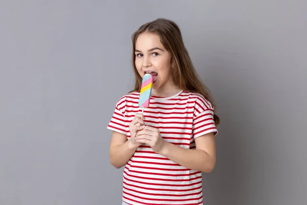 Portrait Delighted Cute Little Girl Wearing Striped Shirt Biting Colorful — Fotografia de Stock