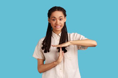 I need more time. Portrait of frustrated woman with black dreadlocks showing time out gesture, looking with imploring eyes, hurry to meet deadline. Indoor studio shot isolated on blue background.