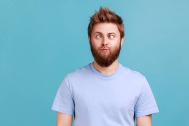 Portrait of man making silly humorous face with eyes crossed, showing comical silly brainless facial expression posing with stupid smile, fooling around. Indoor studio shot isolated on blue background
