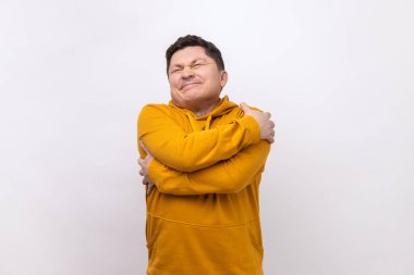 Portrait of selfish narcissistic man embracing himself and smiling with expression of great ego, pleasure and self-esteem, wearing urban style hoodie. Indoor studio shot isolated on white background.