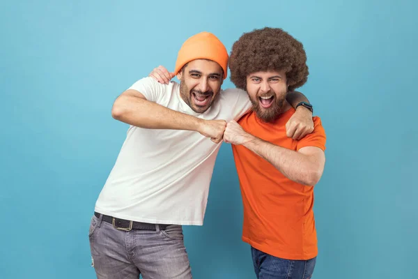 Yes we did. Portrait of two handsome happy excited young adult hipster men celebrating triumph together, showing bro fist, power five sign. Indoor studio shot isolated on blue background.