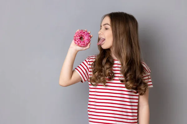 Portrait Hungry Little Girl Wearing Striped Shirt Standing Licking Doughnut — Fotografia de Stock