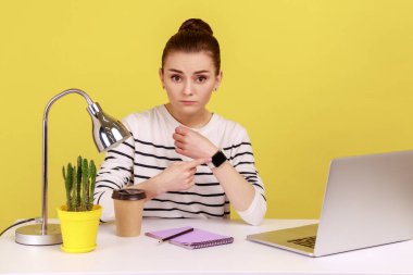 Ciddi bir kadın çalışan ofisinde oturuyor ve elini işaret ediyor, canı sıkkın görünüyor, fazla mesaiden yorgun ve dinlenmeye ihtiyacı var. Sarı arka planda kapalı stüdyo çekimleri.