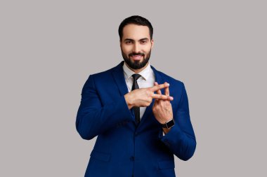 Olumlu iyimser sakallı adam hashtag işareti yapmak için parmaklarını çapraz yapıyor ve kameraya dişlek bir gülümsemeyle bakıyor, resmi stil kıyafeti giyiyor. Gri arka planda izole edilmiş kapalı stüdyo görüntüleri.