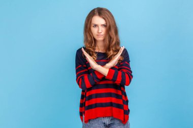 Bu son ve başka yolu yok. Çizgili bir süveter giyen kararlı bir kadının portresi X işaretini çapraz elle gösteriyor, yani dur. Mavi arka planda kapalı stüdyo çekimi.