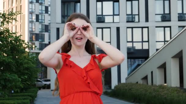 호기심많은 여자가 붉은우아 쌍안경으로 손가락을 응시하며 바라보고 옥외에서 현대식 건물을 — 비디오