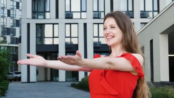 友好的女人穿着红色雅致的衣服 伸出双手给予自由的拥抱 欢迎拥抱 支持和关心 以现代建筑为背景的室外拍摄 — 图库视频影像