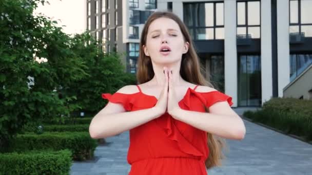长发女人穿着红色雅致的衣服 紧闭双眼 手心紧握 练习瑜伽呼吸技巧 减轻压力 以现代建筑为背景的室外拍摄 — 图库视频影像