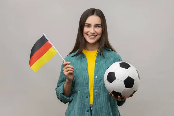 笑容满面的女人手握德国国旗和足球 在锦标赛中支持最受欢迎的球队 穿着休闲风格的夹克 在灰色背景下被隔离的室内拍摄 — 图库照片