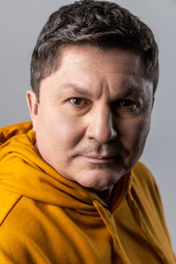 Sakin bir ifadeyle kameraya bakan yakışıklı, kendine güvenen bir adamın yakın portresi, erkek sağlık hizmetleri ve güzellik, şehir tarzı kapüşonlu kapüşon giyiyor. Gri arka planda izole edilmiş kapalı stüdyo görüntüleri.