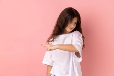 Get out. Portrait of little girl wearing white T-shirt showing exit, demanding to leave her alone, turning away with resentful irritated expression. Indoor studio shot isolated on pink background. clipart