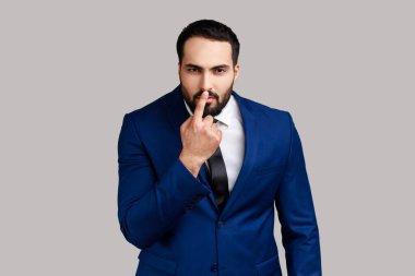 Şüpheci bakışlar atan ve burnuna dokunan sakallı bir adam. Yalancısın, yalancılıktan kuşkulanıyorsun, resmi tarz takım elbise giyiyorsun. Gri arka planda izole edilmiş kapalı stüdyo görüntüleri.